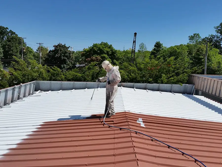 Professional roofer spraying seal coating onto commercial building's roof - Madison County, Illinois